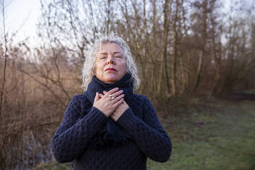 Senior woman with eyes closed praying in front of bare tree - FVDF00356