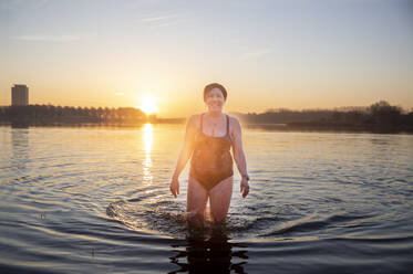 Lächelnde reife Frau im Wasser stehend am Morgen - FVDF00401