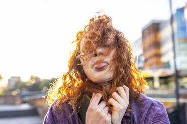 Curly haired woman sticking out tongue during sunset - WPEF05062