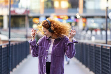 Woman wearing headphones dancing on bridge - WPEF05066