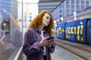 Frau mit Mobiltelefon wartet am Bahnhof auf die Straßenbahn - WPEF05075