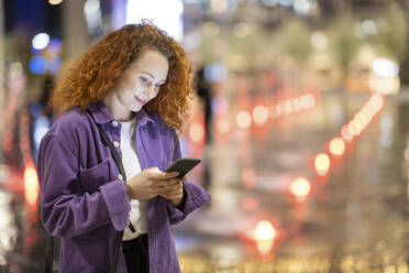 Schöne junge Frau, die nachts ein Mobiltelefon benutzt - WPEF05085