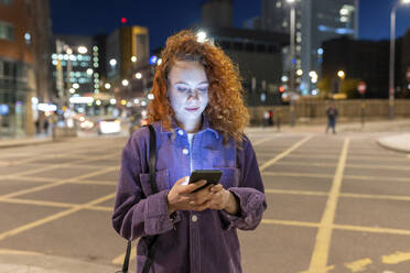 Junge Frau benutzt ihr Smartphone auf einer nächtlichen Kreuzung - WPEF05087