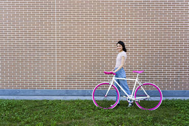 Lächelnde junge Frau mit Fahrrad an der Mauer - GIOF13033