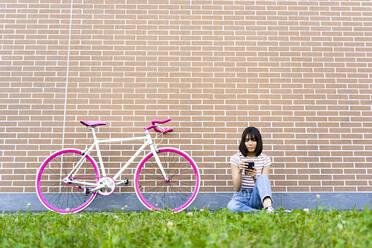 Frau mit kurzen Haaren benutzt ihr Smartphone auf dem Fahrrad auf dem Gehweg - GIOF13047