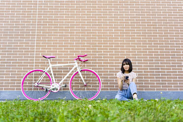 Junge Frau mit Mobiltelefon auf dem Fahrrad sitzend auf dem Fußweg - GIOF13048