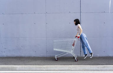 Frau mit kurzen Haaren spielt mit einem Einkaufswagen auf dem Gehweg - GIOF13058
