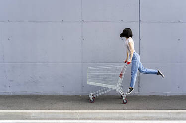 Junge Frau hat Spaß mit Einkaufswagen auf dem Fußweg - GIOF13059