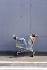 Woman with hands behind head relaxing in shopping cart - GIOF13065
