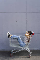 Woman sleeping in shopping cart on footpath - GIOF13066