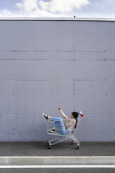 Young woman taking selfie on mobile phone while sitting in shopping cart - GIOF13070