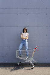 Smiling woman with arms crossed standing in shopping cart - GIOF13080