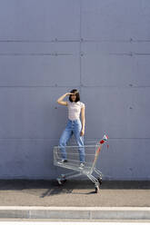 Woman shielding eyes while standing in shopping cart - GIOF13082