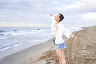 Carefree woman with arms outstretched standing at beach - VEGF04733