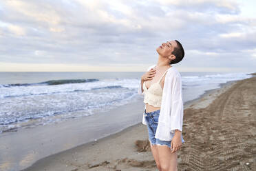 Smiling woman standing with eyes closed at beach - VEGF04734