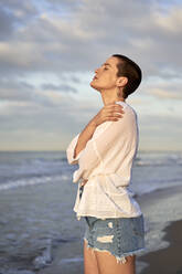 Frau umarmt sich selbst, während sie am Strand steht - VEGF04745