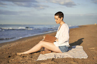 Woman writing in diary while sitting on blanket - VEGF04752