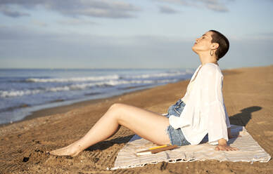 Woman relaxing while sitting on blanket at beach - VEGF04753