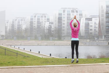Frau mit erhobenen Händen springt beim Sport im Park - FVDF00417