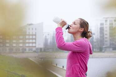 Woman drinking water at park in city - FVDF00429