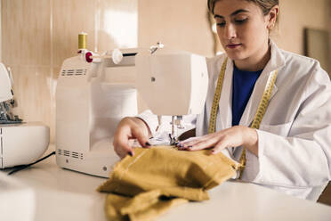 Young female tailor using sewing machine at workbench - GRCF00778