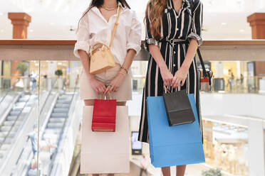 Freundinnen halten Einkaufstüten, während sie vor einem Glasgeländer stehen - JRVF01210