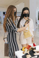 Female friends in face masks checking sandal while shopping at mall - JRVF01228