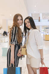 Lächelnde Freundinnen, die Einkaufstüten halten, während sie in einem Einkaufszentrum stehen - JRVF01246