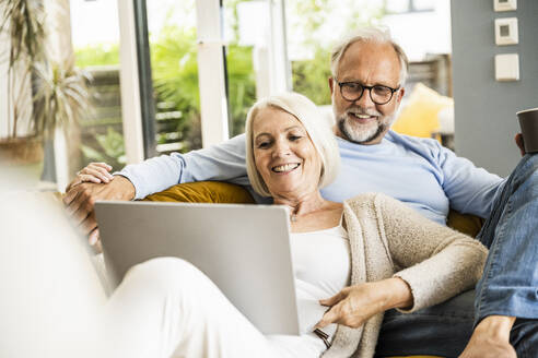 Älteres Paar lächelt während eines Videoanrufs über einen Laptop im Wohnzimmer - UUF24073