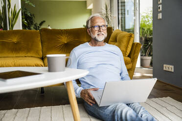 Mature man with laptop sitting on floor at home - UUF24080
