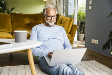 Man using laptop while sitting on floor in living room - UUF24081