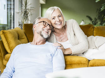 Smiling mature woman leaning on man while resting on sofa - UUF24086