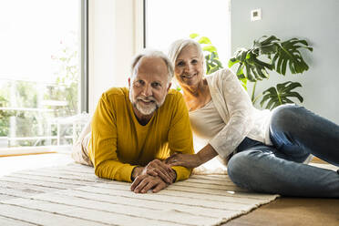 Smiling mature couple resting together on carpet at home - UUF24105