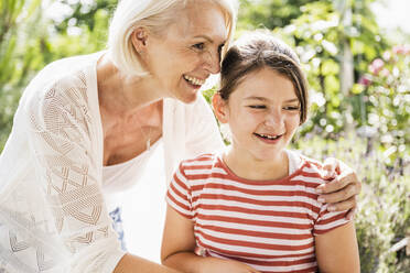 Smiling grandmother standing with arm around granddaughter - UUF24114