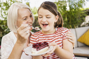 Großmutter füttert ihre Enkelin auf dem Balkon mit Kuchen - UUF24118
