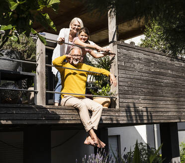 Großeltern und Enkelin lächelnd auf dem Balkon an einem sonnigen Tag - UUF24123