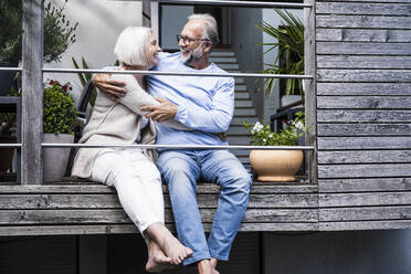 Smiling woman embracing man while sitting at balcony - UUF24135