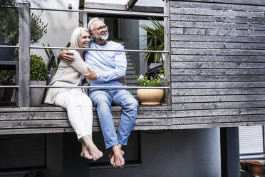 Thoughtful couple embracing while sitting together at balcony - UUF24137