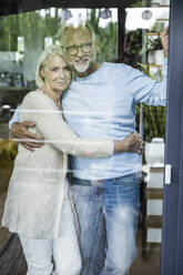 Smiling man standing with arm around of woman behind glass door - UUF24153