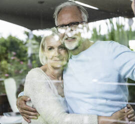 Couple embracing while standing behind glass window - UUF24154