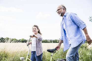 Lächelnder Großvater mit Fahrrad und Enkelin auf der Wiese - UUF24158