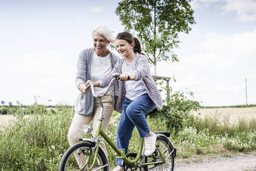 Smiling woman teaching girl riding bicycle on dirt road - UUF24161