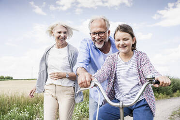 Smiling grandparents playing with granddaughter riding bicycle - UUF24165