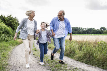 Fröhliche Großeltern spielen mit ihrer Enkelin, während sie auf einem Feldweg laufen - UUF24175
