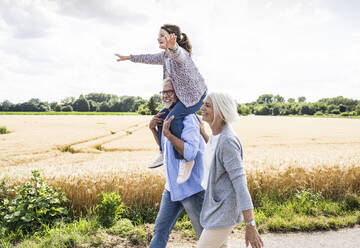 Grandparents walking with playful granddaughter during sunny day - UUF24188