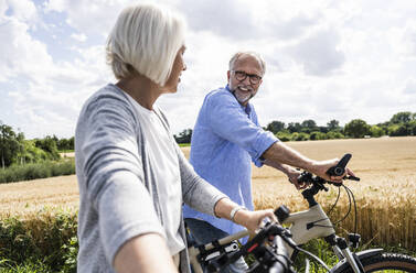 Mann im Gespräch mit Frau beim Spaziergang mit Fahrrad an einem sonnigen Tag - UUF24190