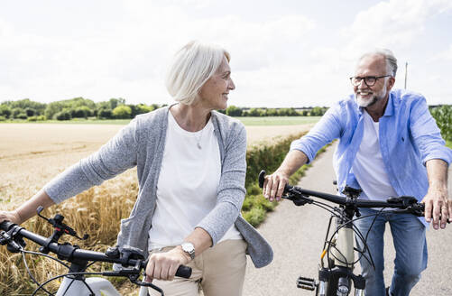 Smiling woman looking at man while walking with bicycles on road - UUF24193