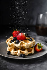 Puderzucker fällt auf einen Teller mit frischen Waffeln mit Erdbeeren und Blaubeeren - FLMF00617