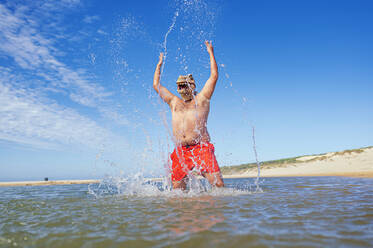 Älterer Mann spritzt Wasser, während er im Urlaub Spaß im Meer hat - JCMF02174