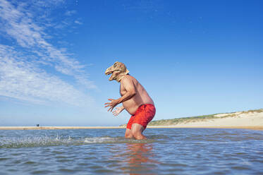 Mann mit Eidechsenmaske gestikuliert im Meer am Strand - JCMF02175